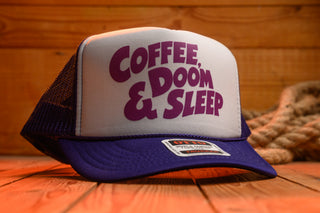 Trucker hat with 'Coffee, Doom & Sleep' text on a wooden surface